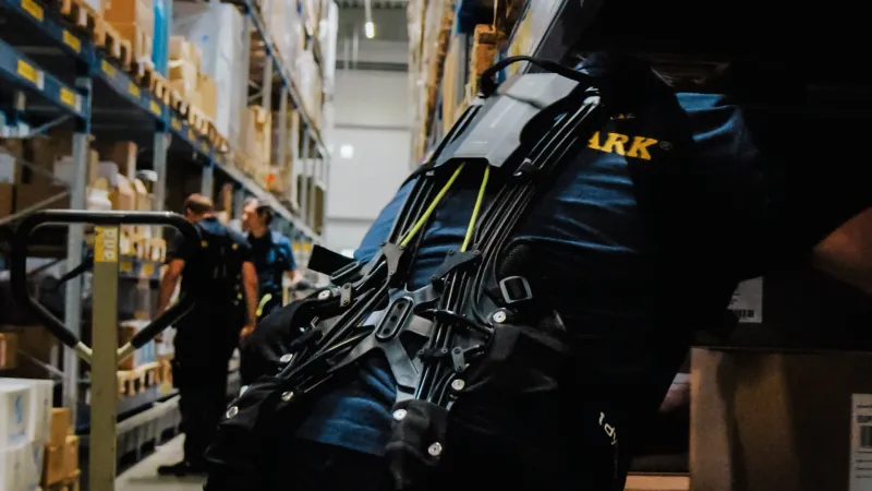 Mann kommissioniert mit Exoskelett im Lager vom Europark